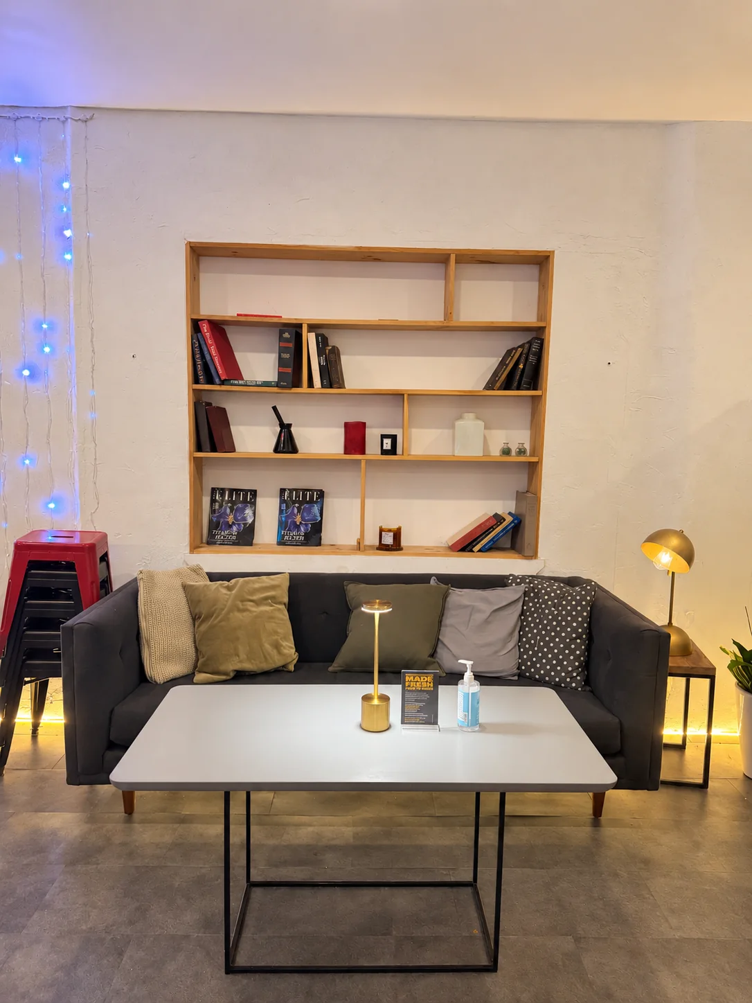 A sofa with cushions, a low table and brass lamps beneath a wooden bookshelf at Chicken Is Back