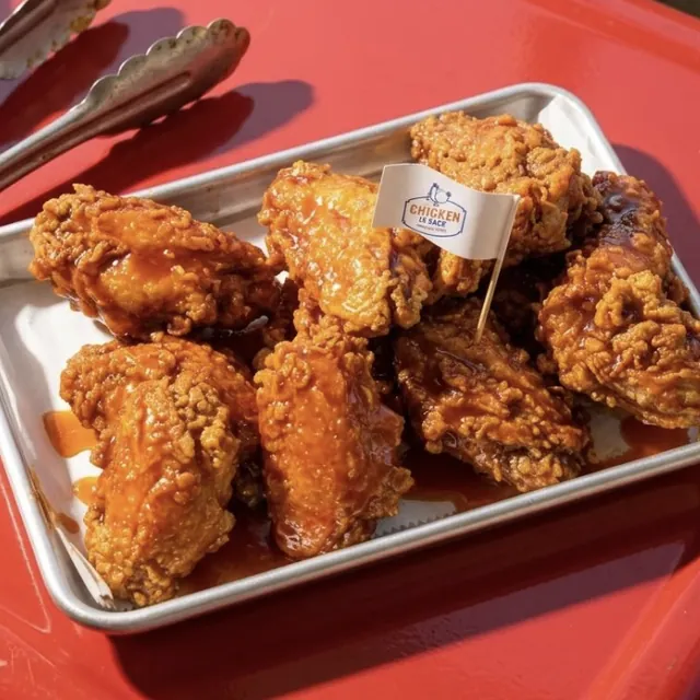 A tray of red pepper wings with tongs on a red table
